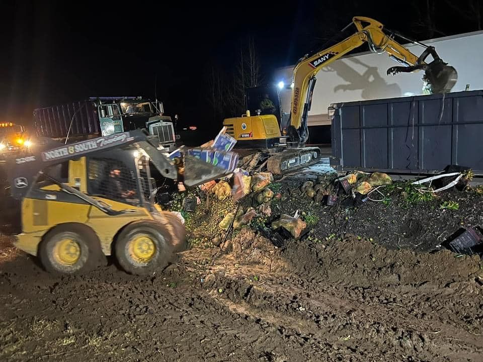 Construction scene at night: Excavators and a skid steer removing debris next to a building and a truck.