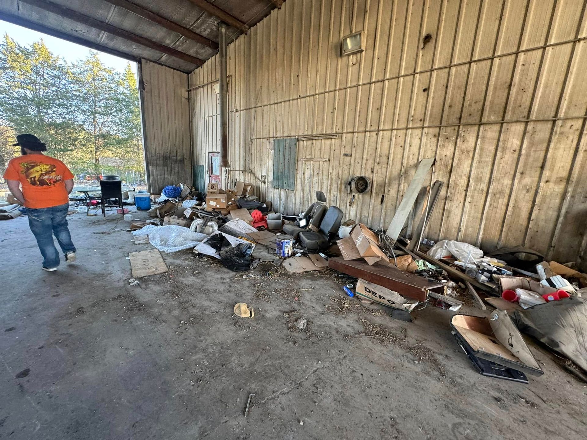 Person walking past a cluttered, open-sided shed filled with debris and automotive parts.