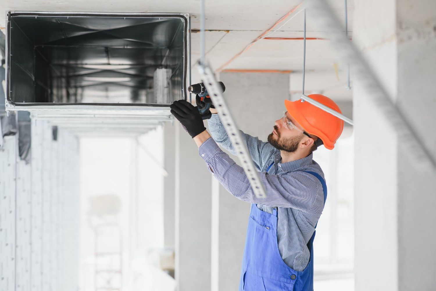 A man is working on a ventilation system in a building.