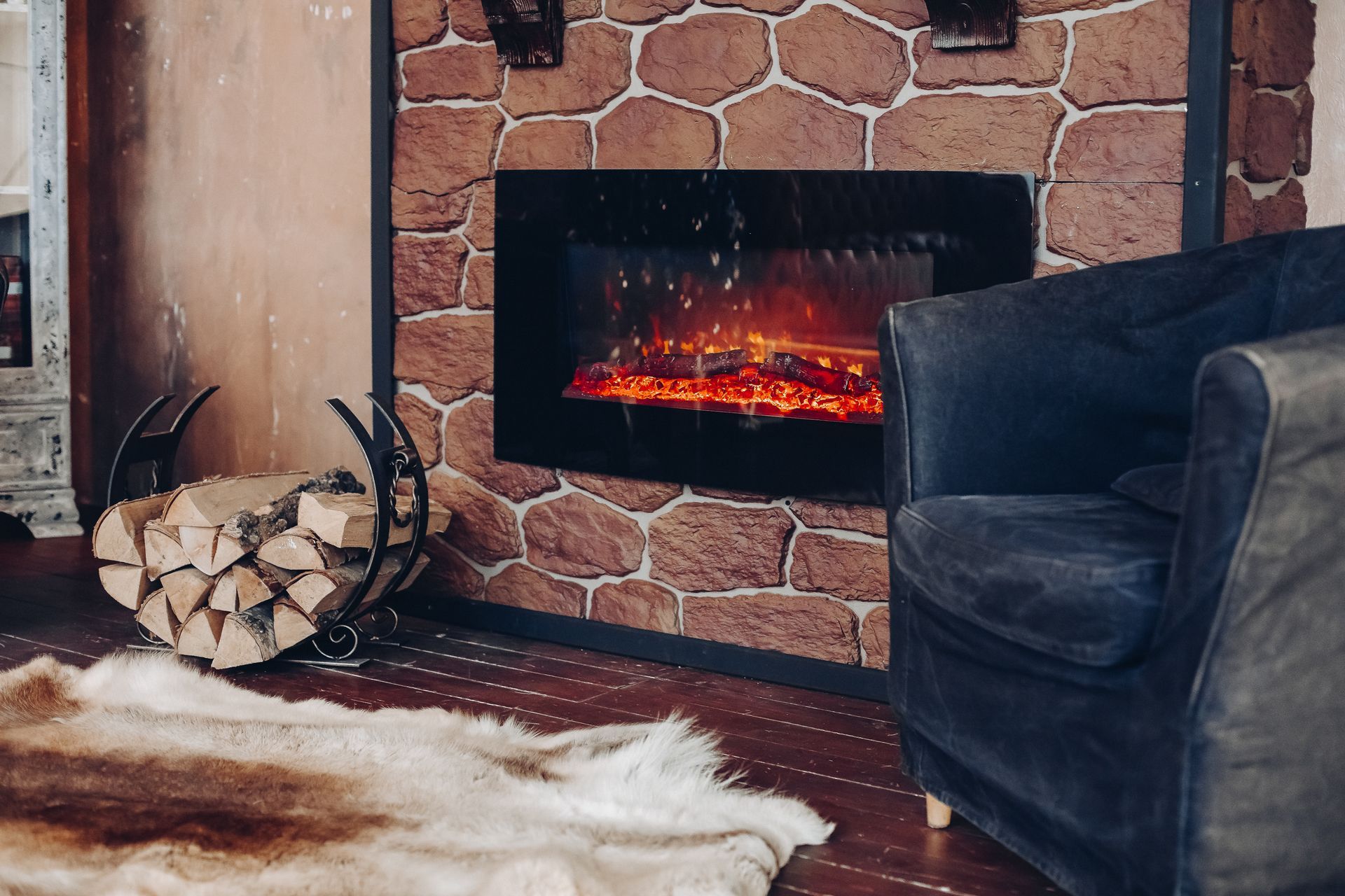 Cozy living room fireplace with glowing fire, dark armchair, wood logs, and white rug