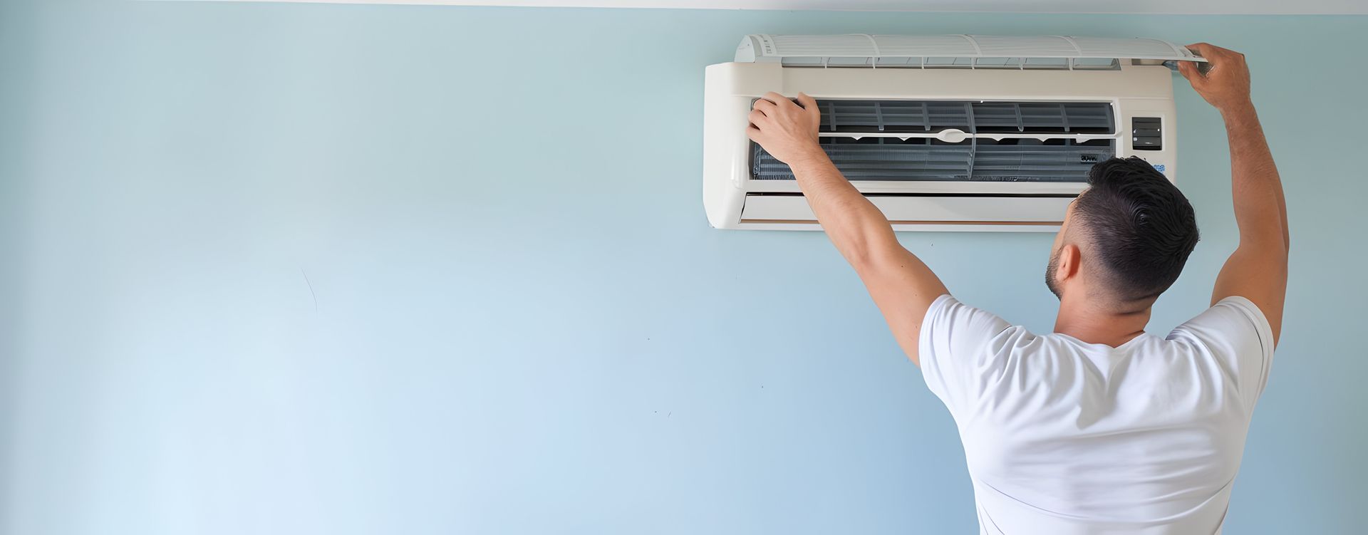 Man installing a wall-mounted air conditioner on a light blue wall