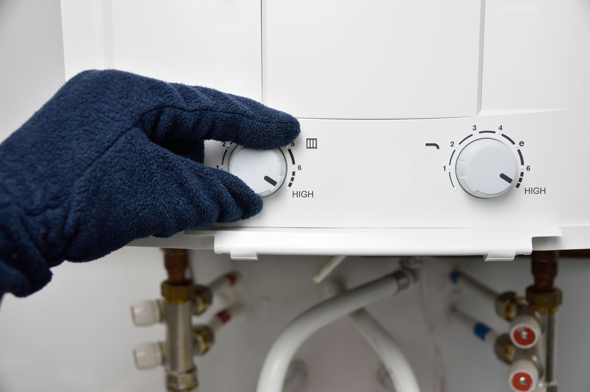 A gloved hand adjusting a dial on a white water heater.