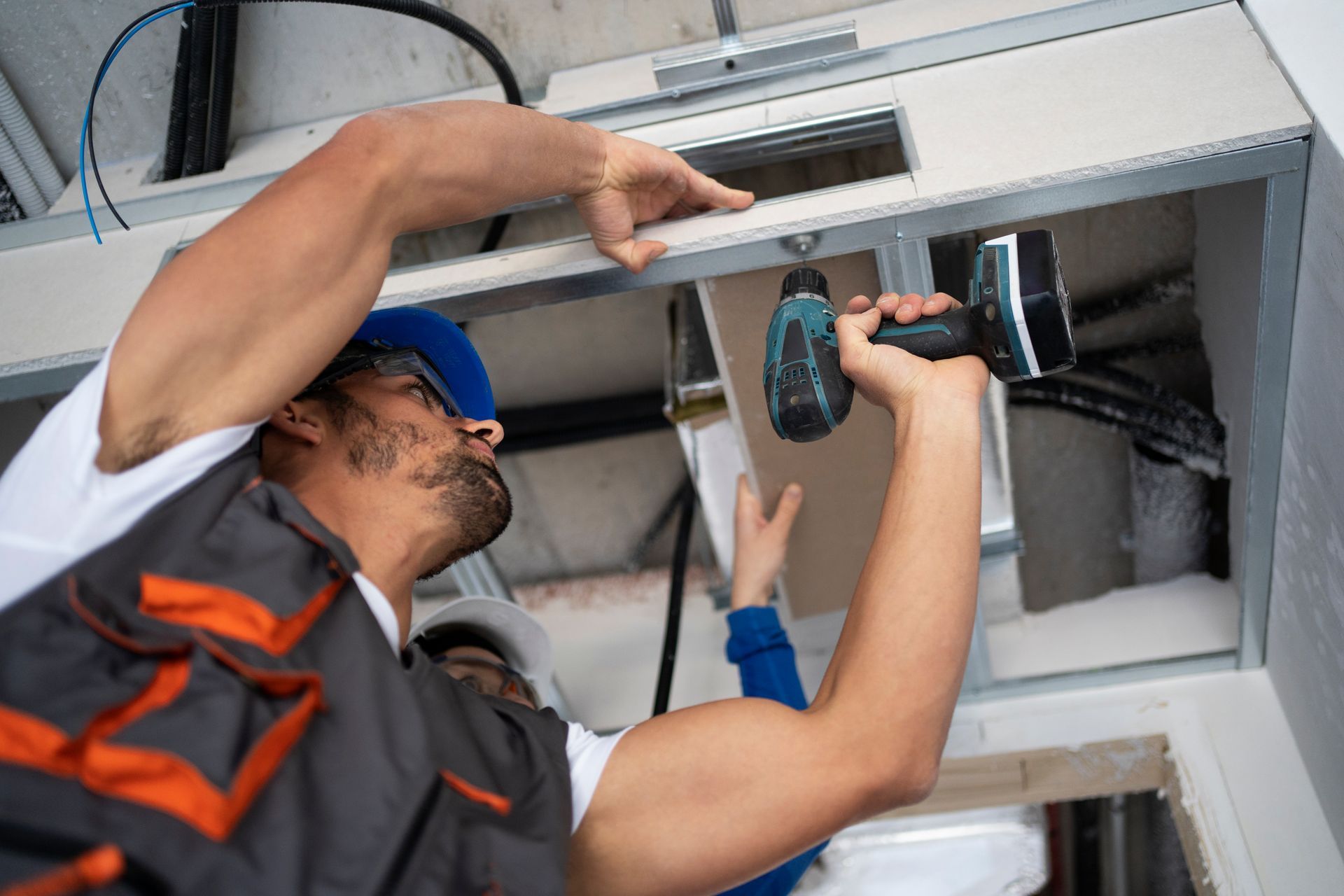 Technicians installing a ceiling vent, using a drill inside an indoor workspace