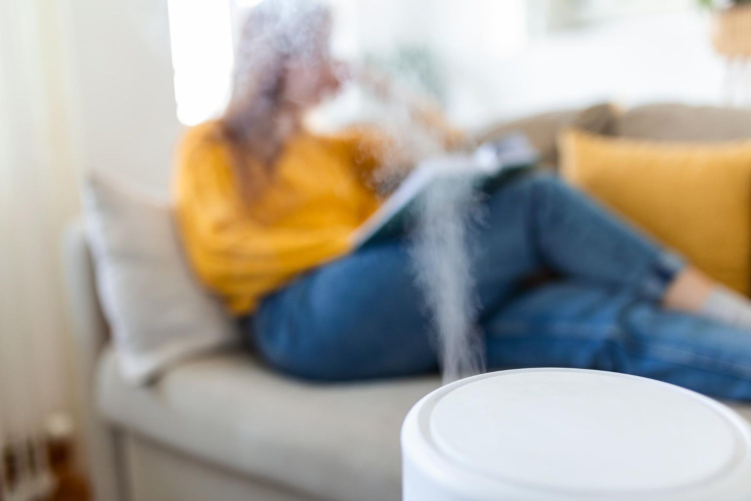 Woman relaxes on couch, humidifier in foreground, misting.