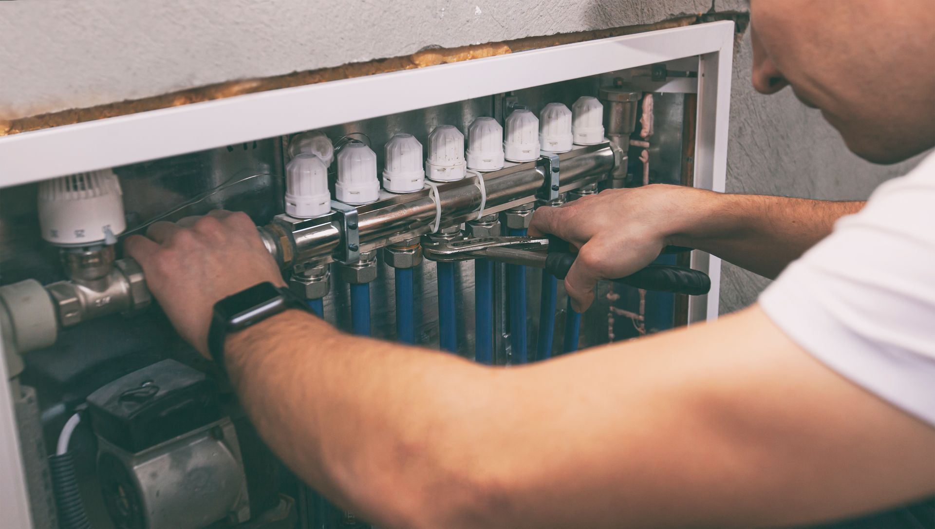 A man is working on a heating system with a wrench.