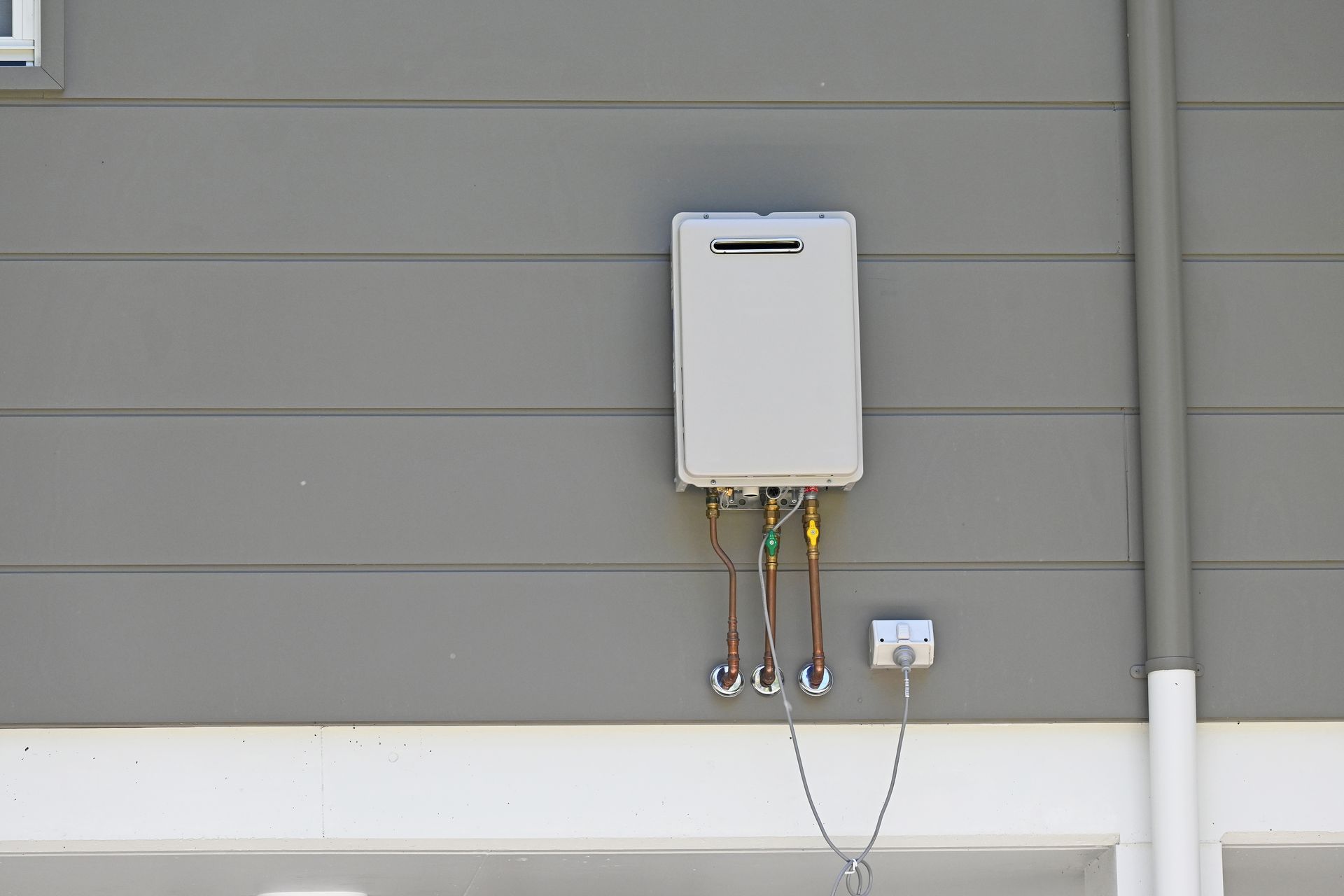 A white water heater is attached to the side of a house.