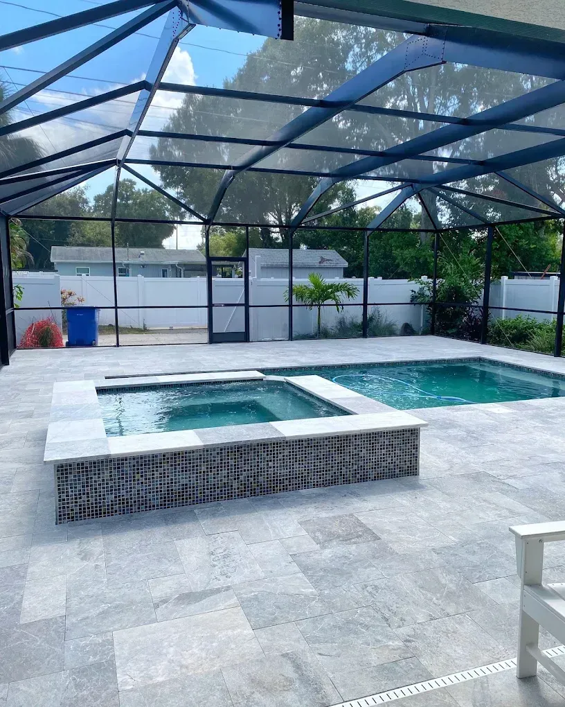 Pool area with pool, hot tub, blue-tiled water, gray pavers, enclosed in a screened enclosure.