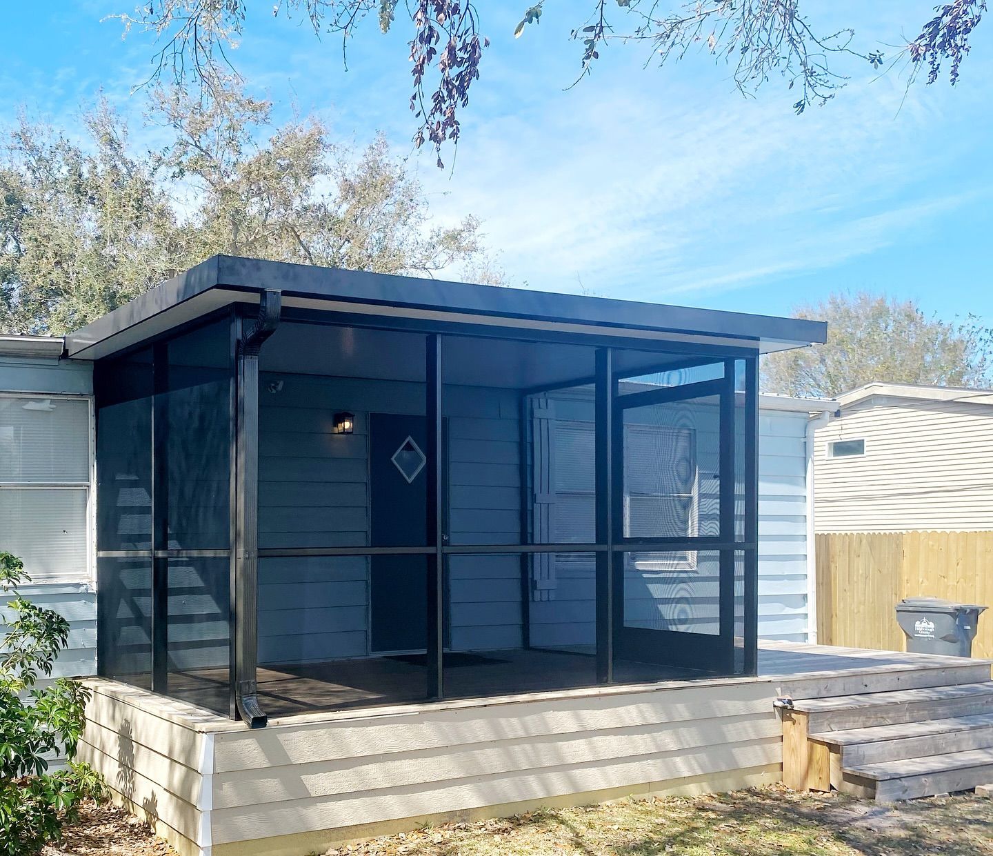 Screened porch addition with black frames and a dark door; on a house with gray siding.