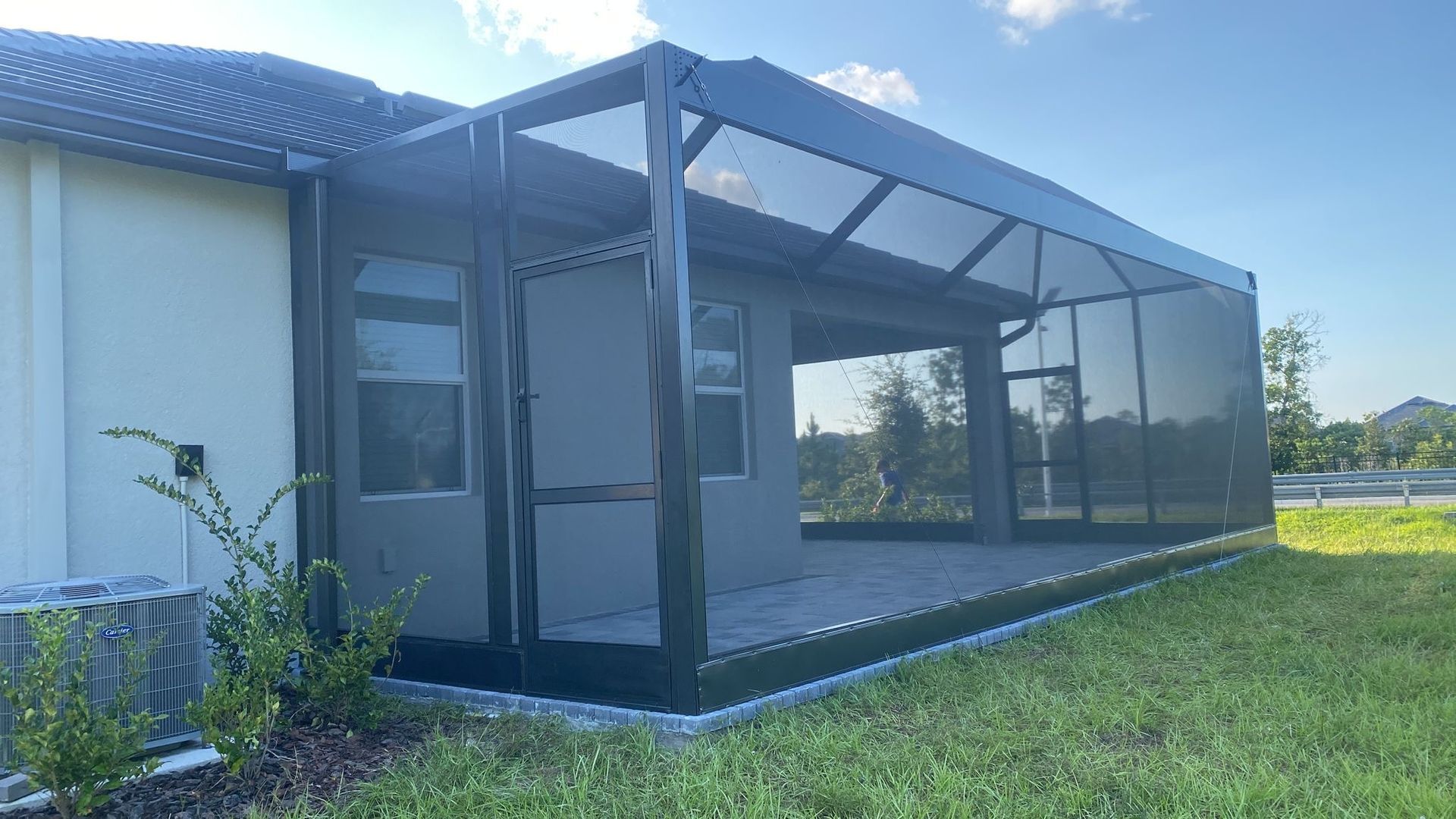 Screened-in patio attached to a white house with green lawn and bushes; overcast sky.