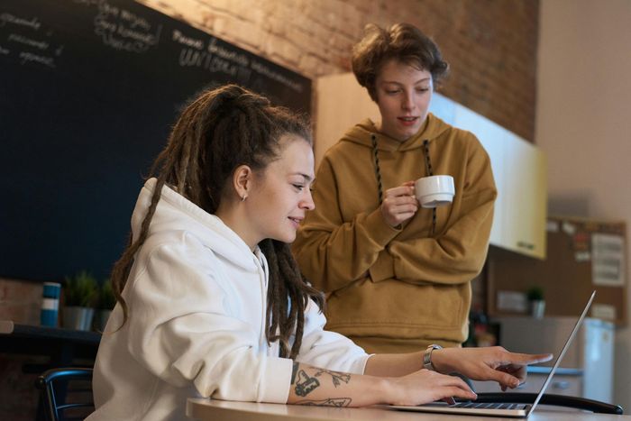 A man is standing next to a woman using a laptop computer.