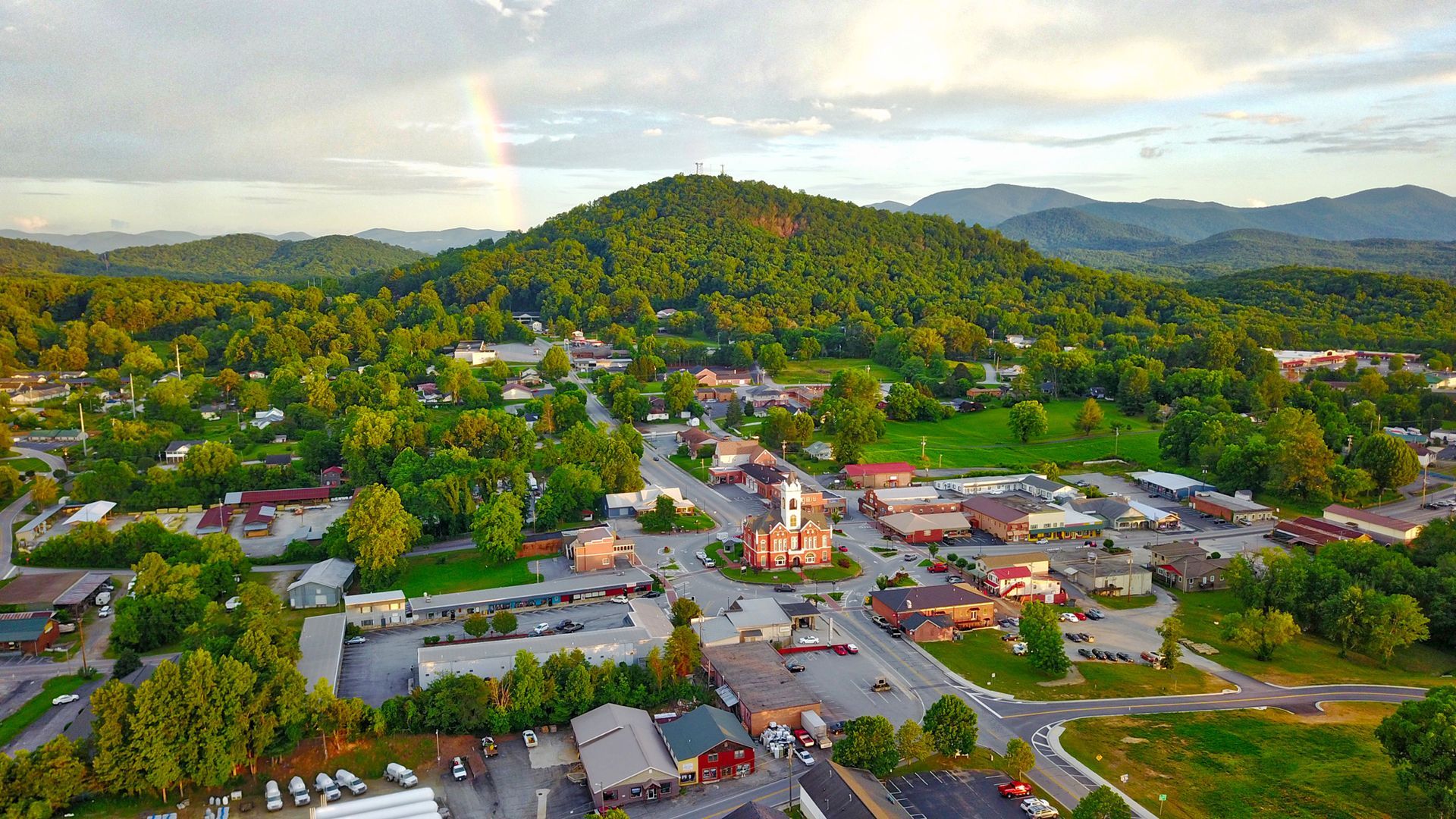 An aerial view of a small town in the mountains with a rainbow in the sky.