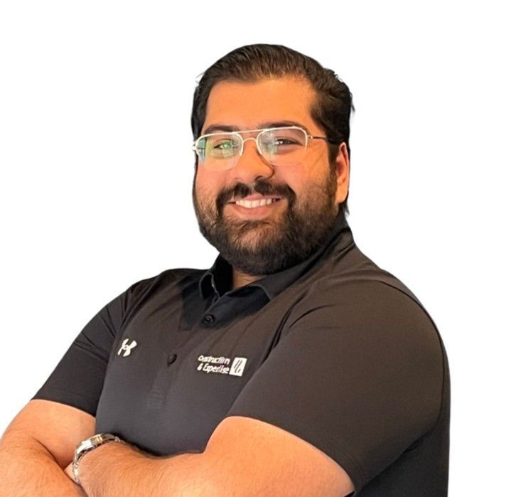 Personne souriante portant des lunettes et une barbe, vêtue d'un polo noir, les bras croisés sur fond blanc
