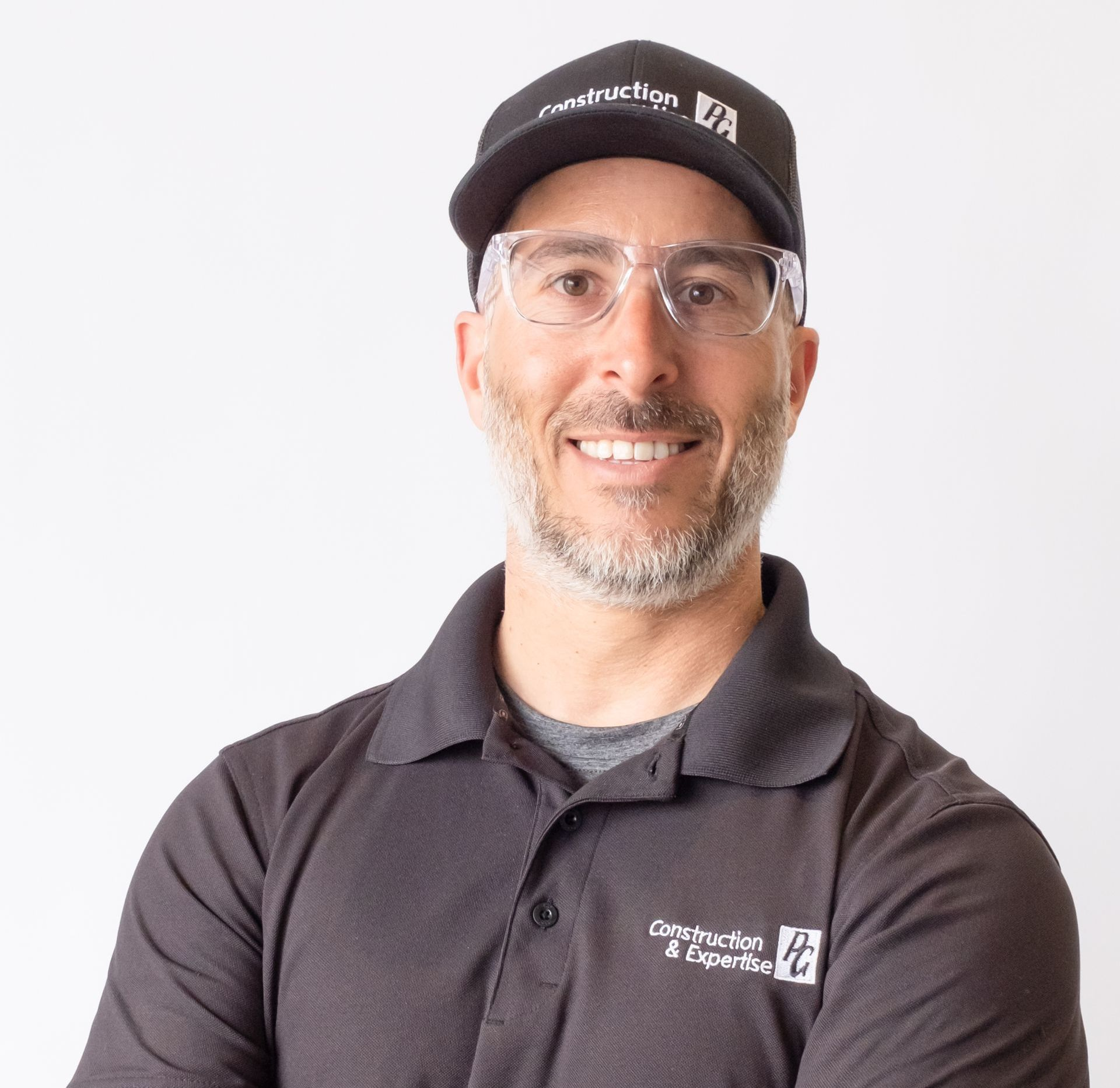 Personne souriante en polo et casquette foncés, portant des lunettes, sur fond blanc uni