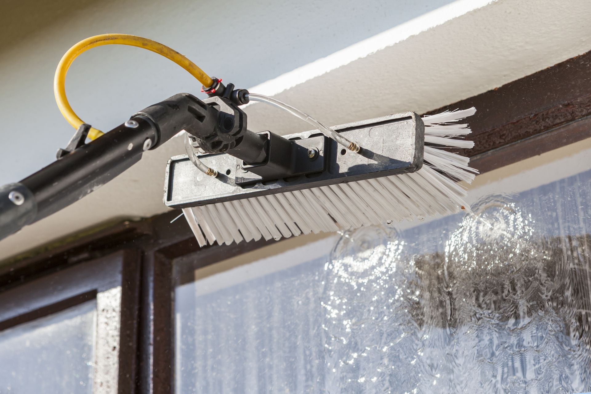 A person cleaning a window with a long-handled brush and water spray.