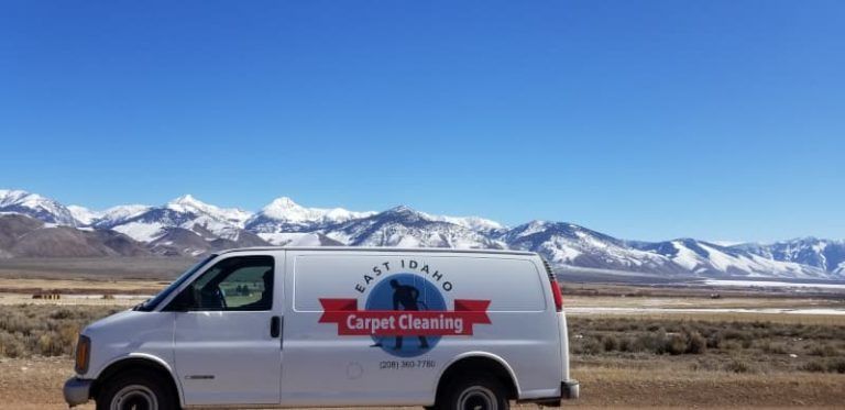 A white van is parked in the middle of a desert with mountains in the background.