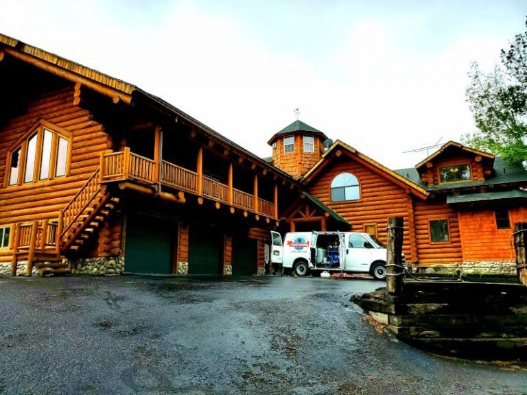 A large log cabin with a white van parked in front of it