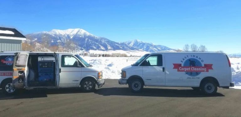 Two white vans are parked next to each other in front of a snowy mountain.
