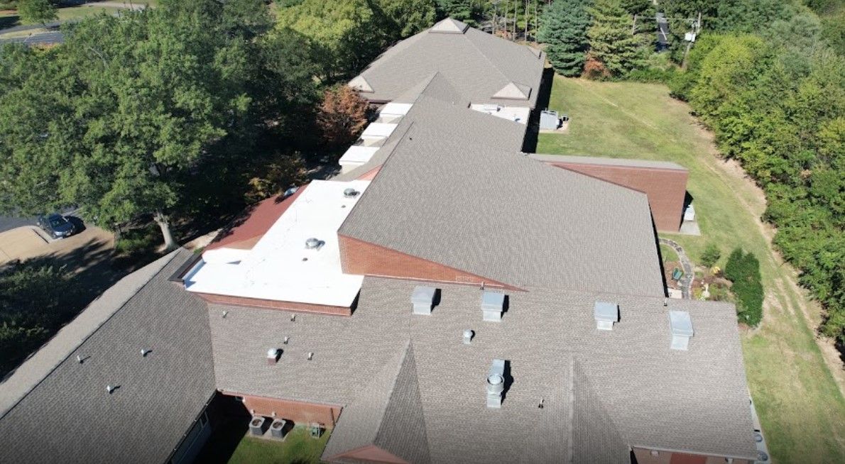 An aerial view of a large house with a white roof surrounded by trees.