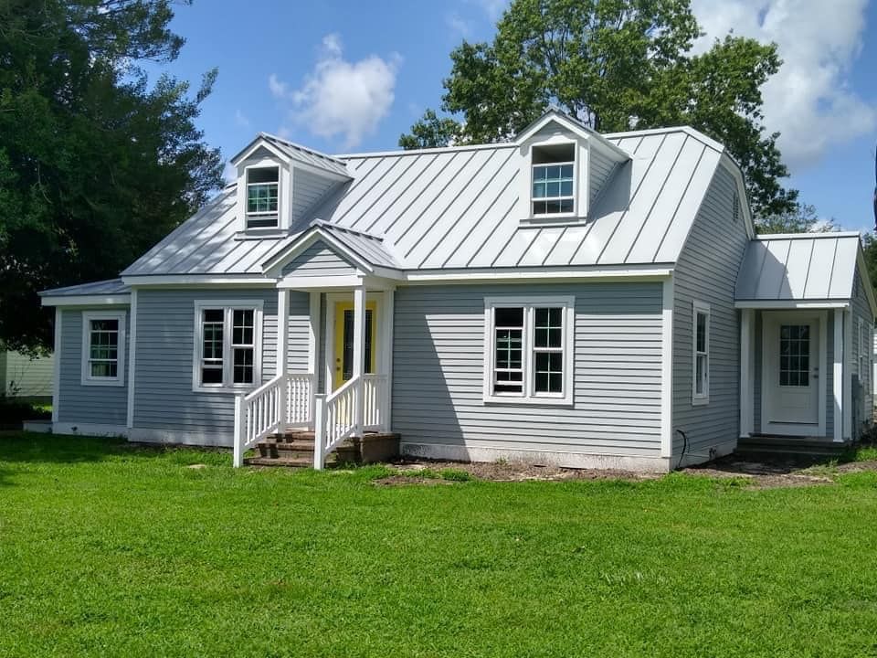 A house with a metal roof is sitting on top of a lush green field.