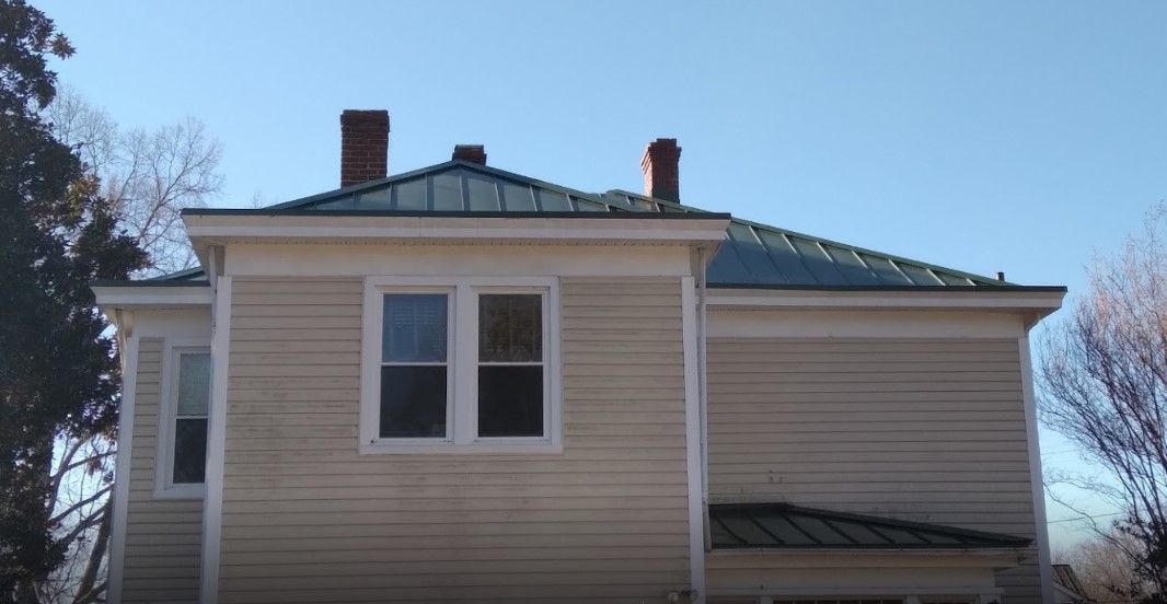 A large white house with a green roof and two chimneys.