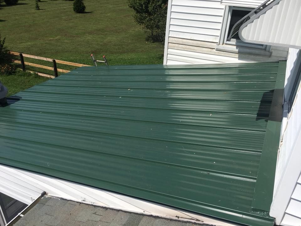 A green metal roof is sitting on top of a white house.