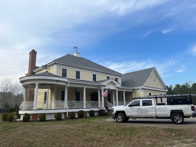 A white truck is parked in front of a large yellow house.