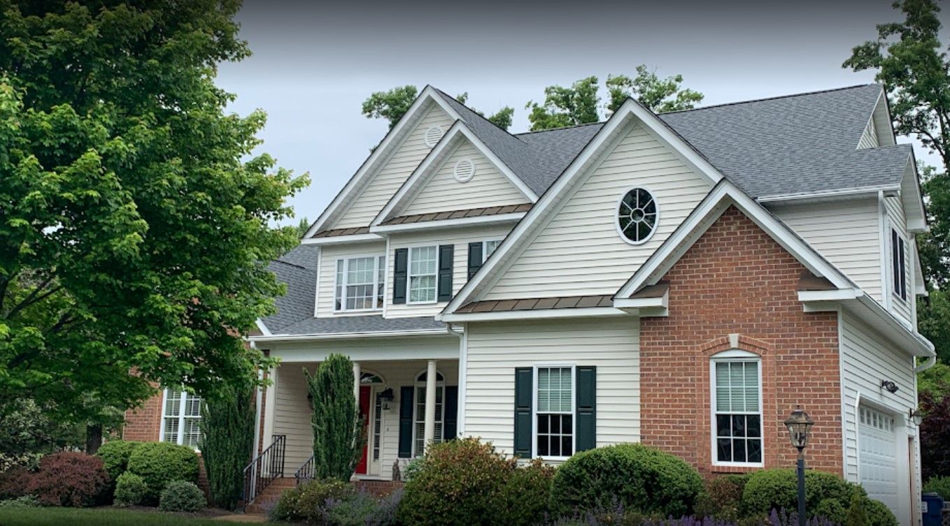 A large white and brick house with a gray roof and black shutters.