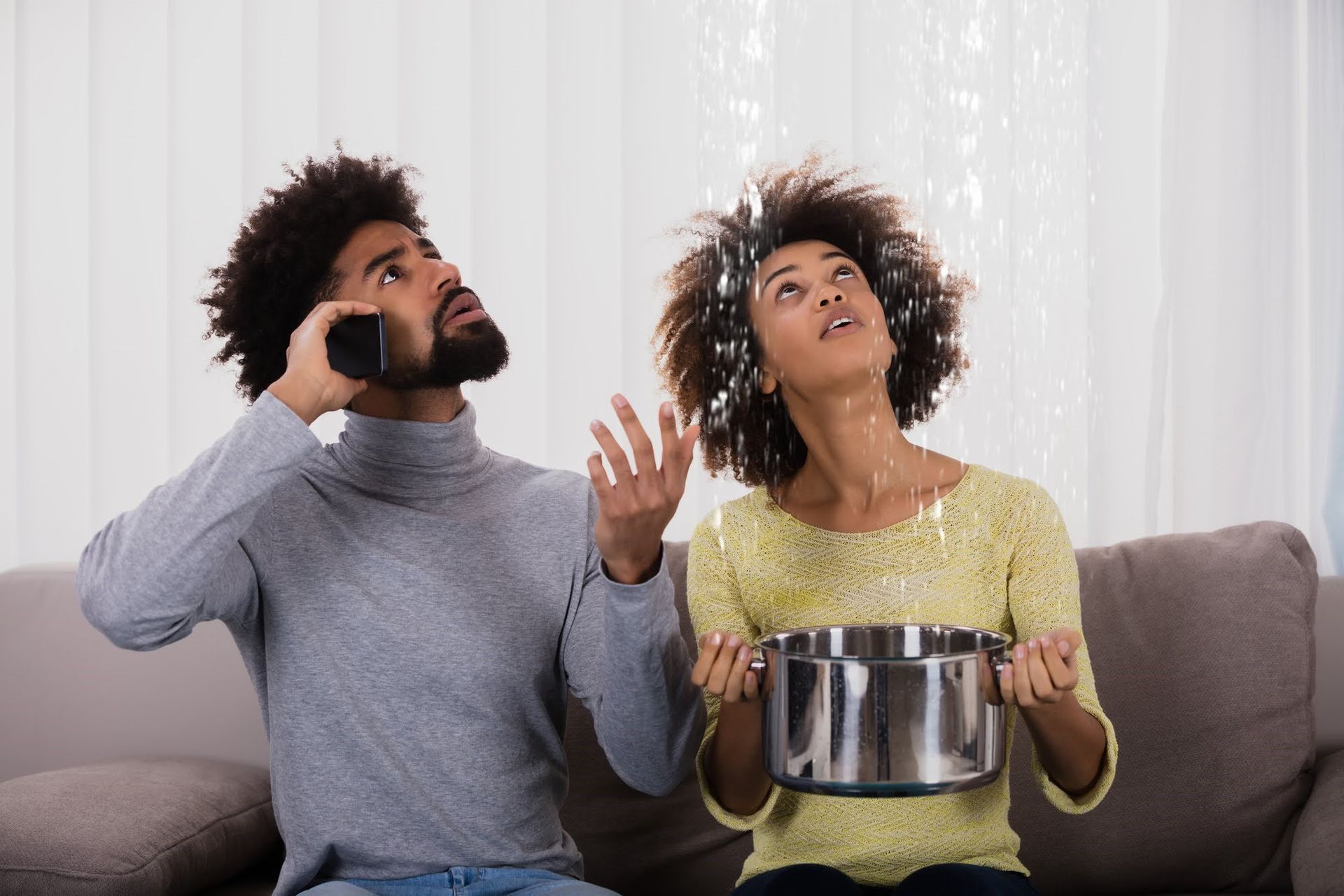 A man and a woman are sitting on a couch looking up at the ceiling.