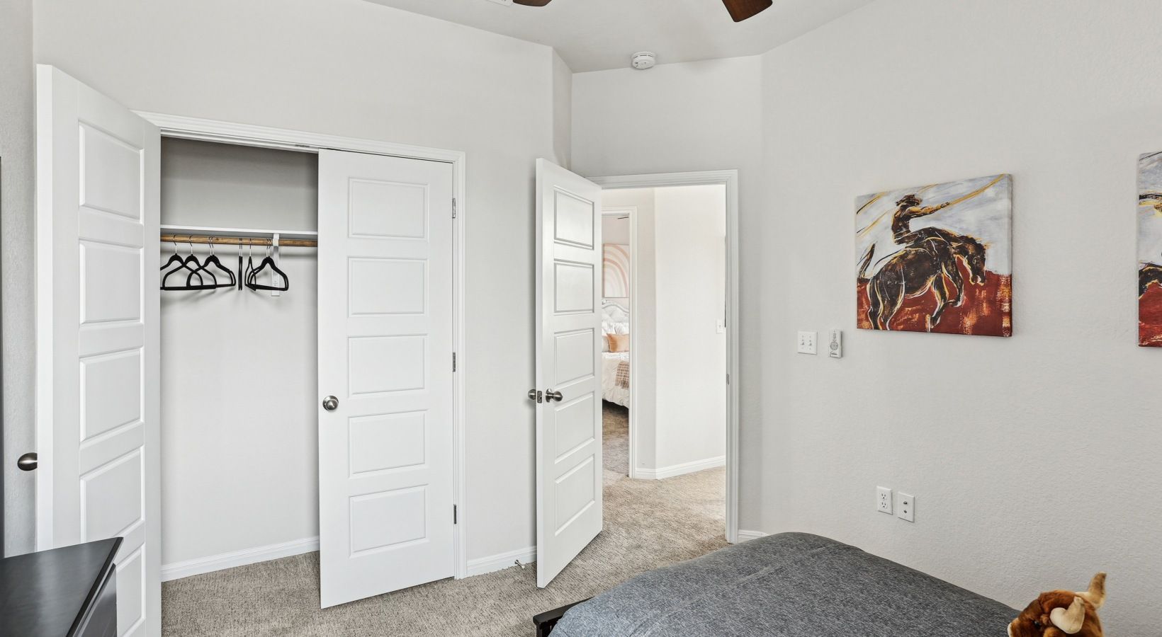 Bedroom with open closet doors, white trim, and neutral decor; bed partially visible.