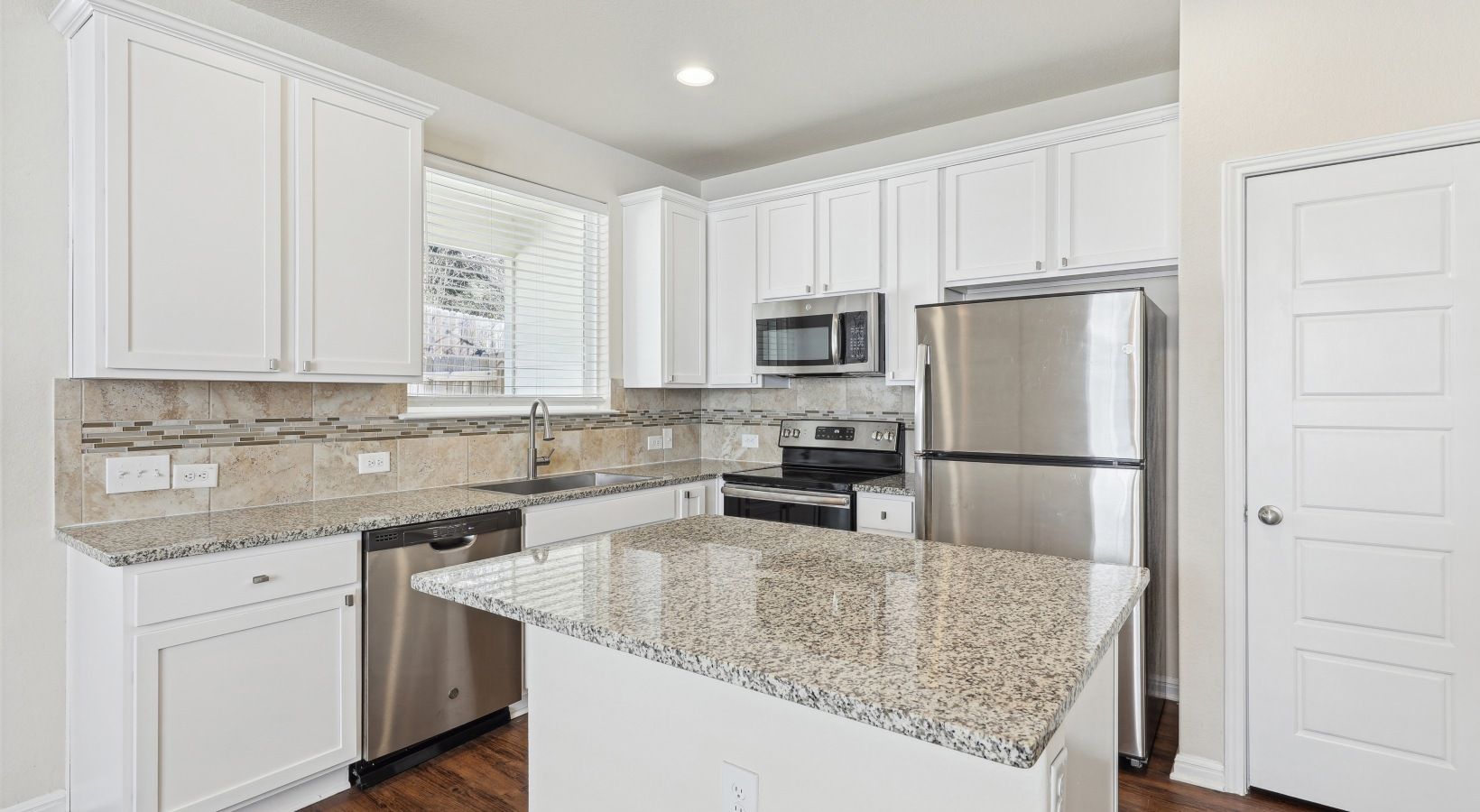 Bright white kitchen with granite countertops, stainless-steel appliances, and an island.