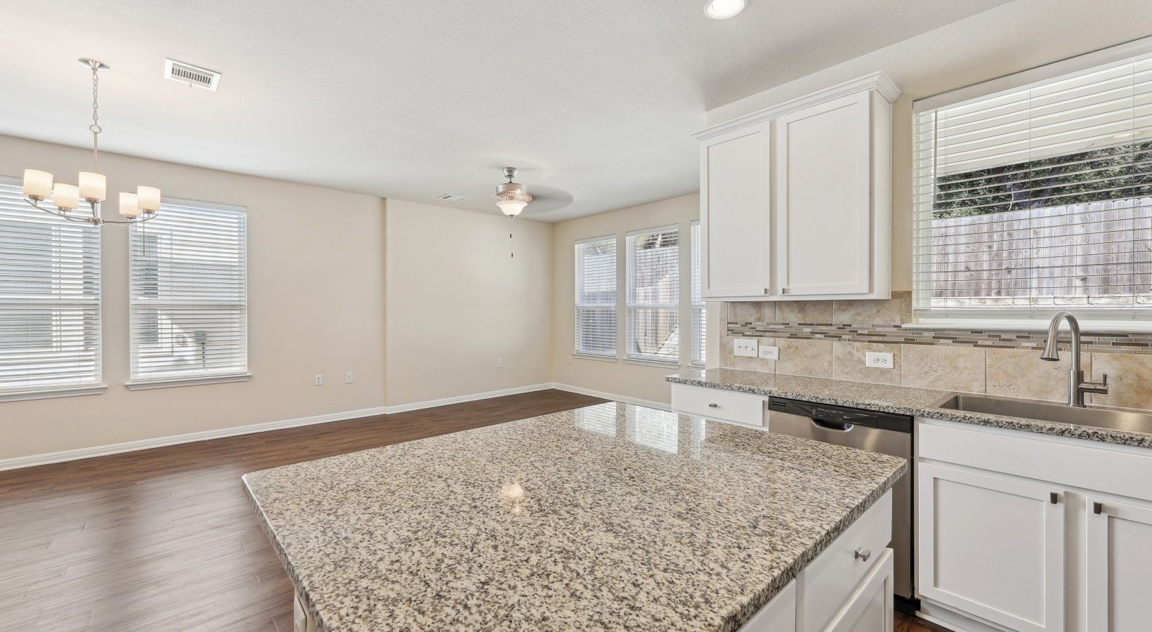 Open kitchen with granite island, white cabinets, stainless steel sink, and large windows.