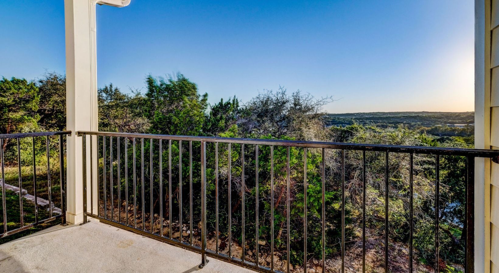 Balcony railing with a scenic treed landscape and distant hills at sunset.