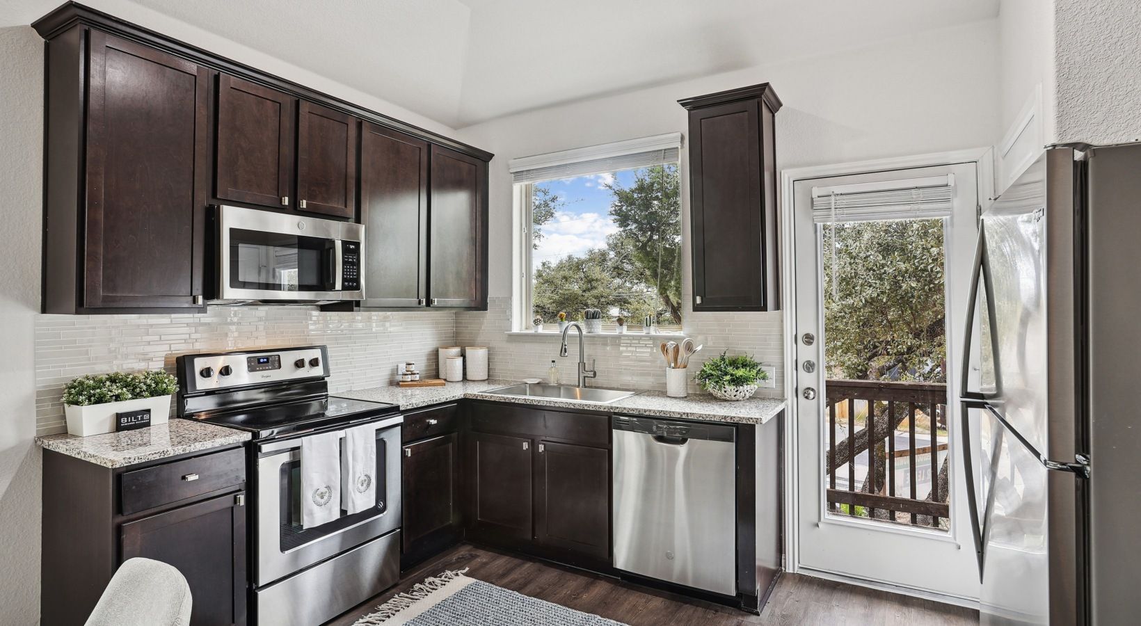 Kitchen with dark wood cabinets, stainless steel appliances, granite counters, and a window above the sink.