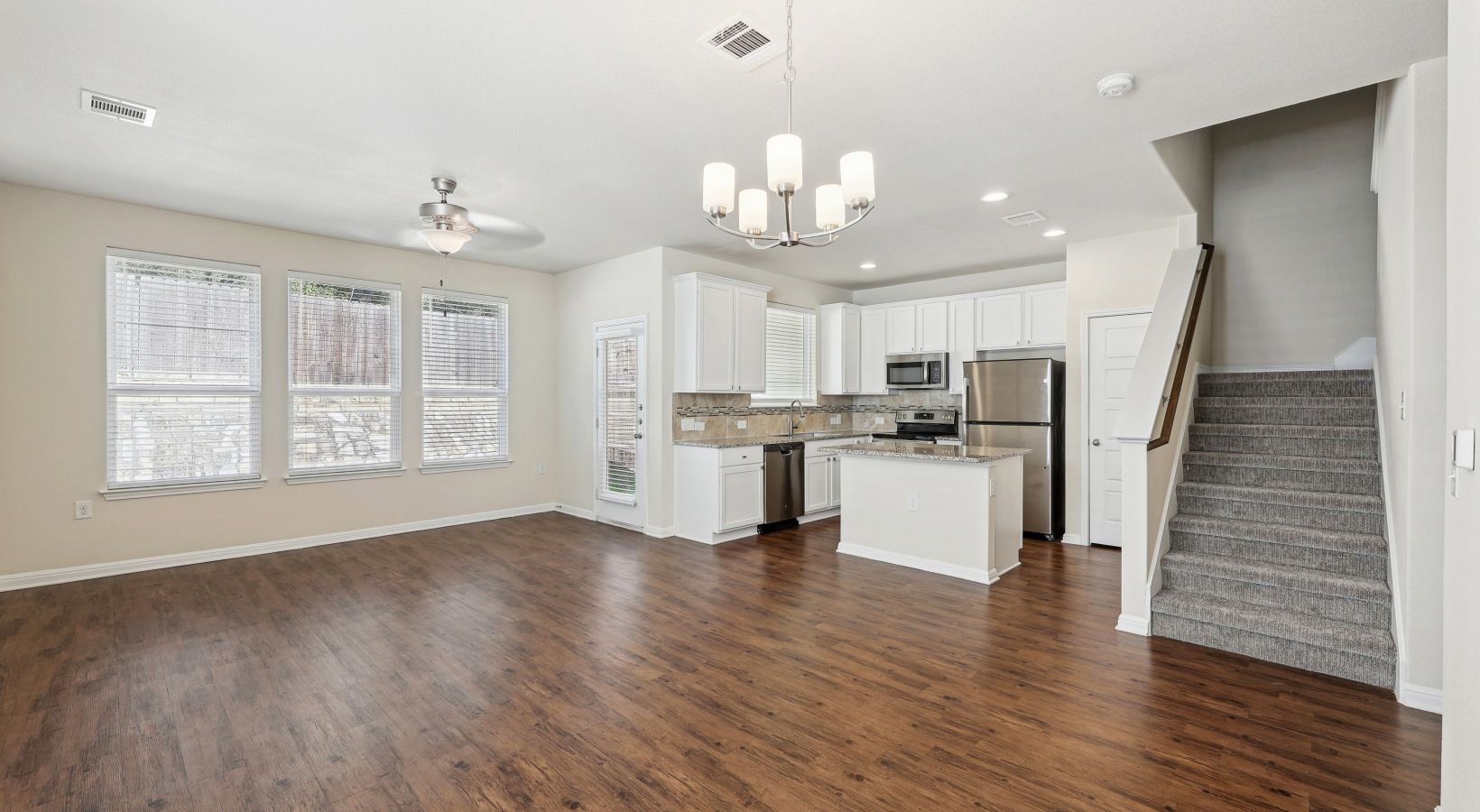Open-concept living area with kitchen island, stainless appliances, white cabinets, and a staircase.