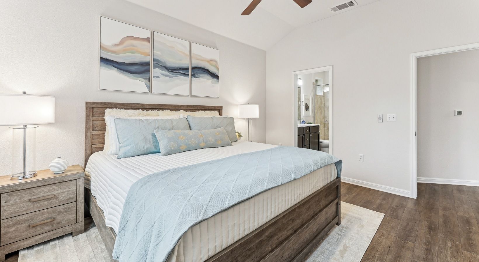 Bedroom with a wooden bed frame, light blue quilt and pillows, two nightstands, and an open bathroom doorway.