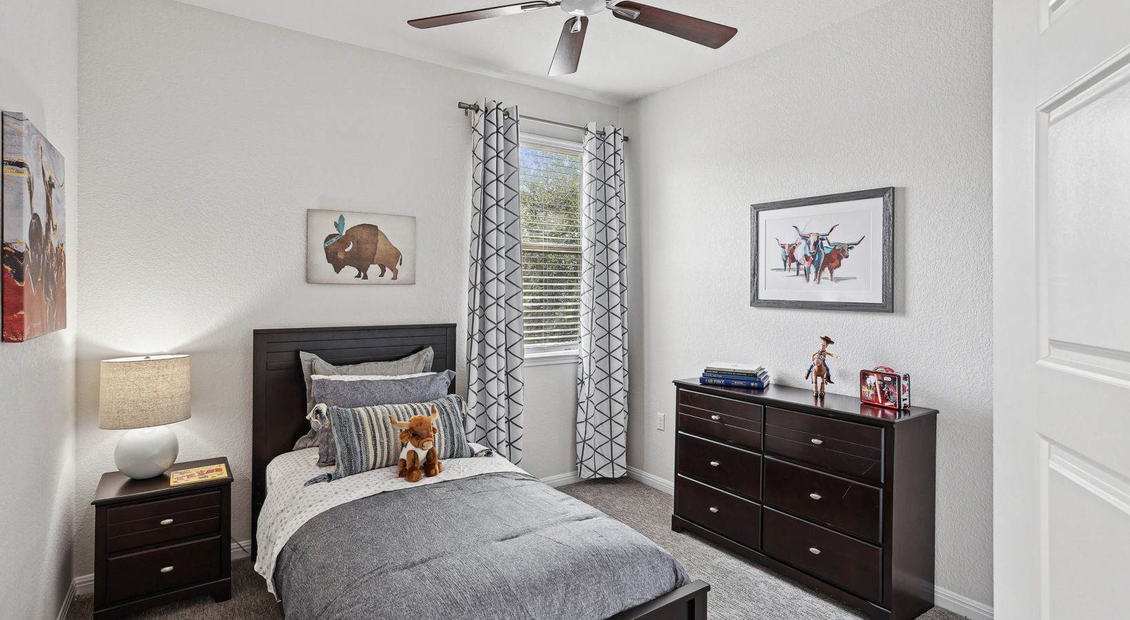 Furnished bedroom with a dark wood bed frame, matching dresser, and a window with geometric-patterned curtains.