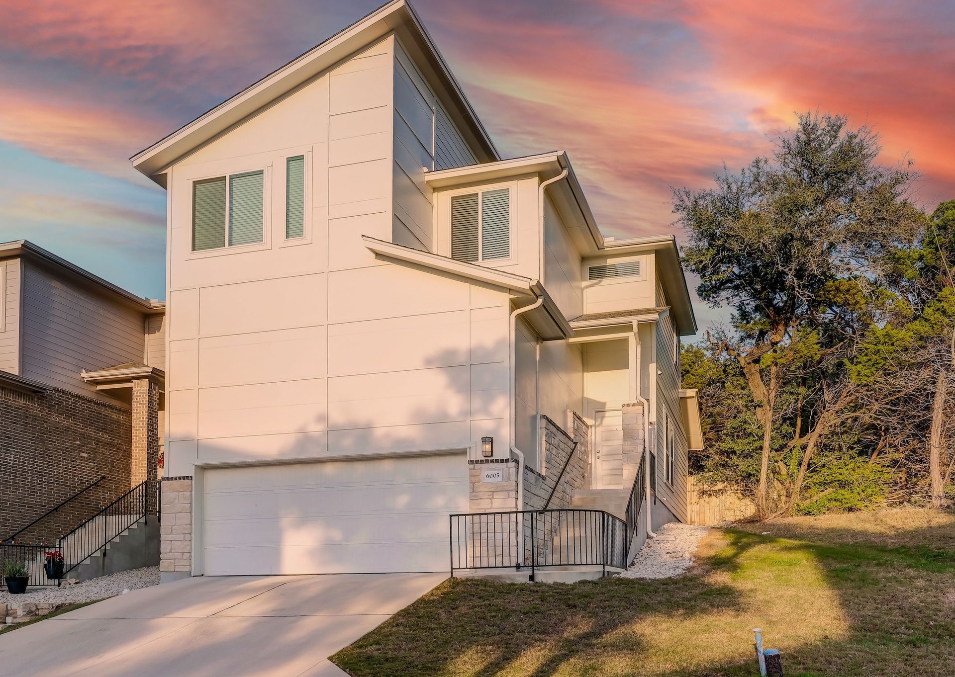 Modern two-story house with a white exterior and a garage, set against a colorful sunset sky.