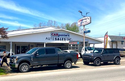 Two trucks are parked in front of a car dealership.