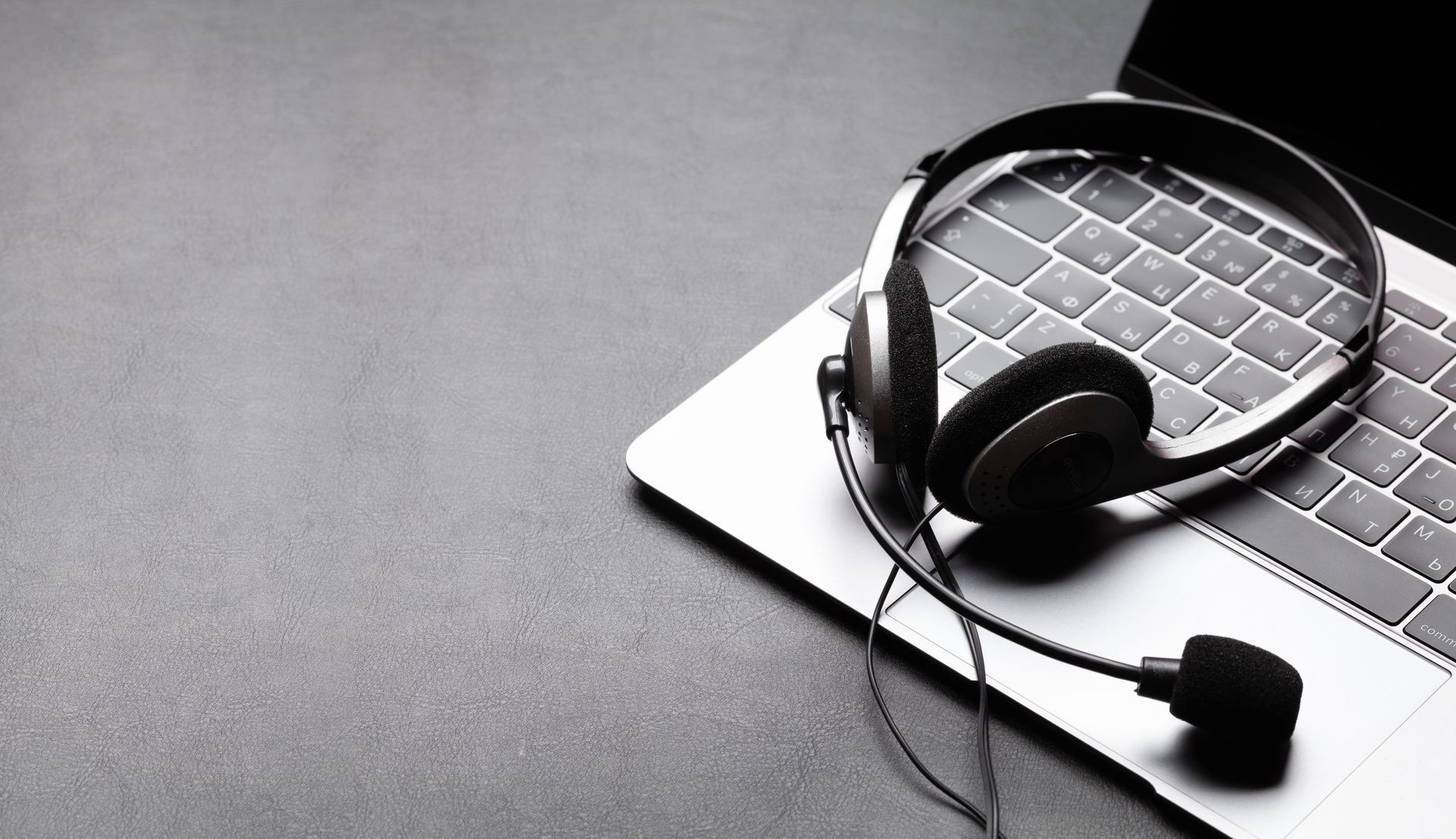 Ein Paar schwarze Over-Ear-Kopfhörer mit Mikrofon, die auf einer silbernen Laptop-Tastatur.
