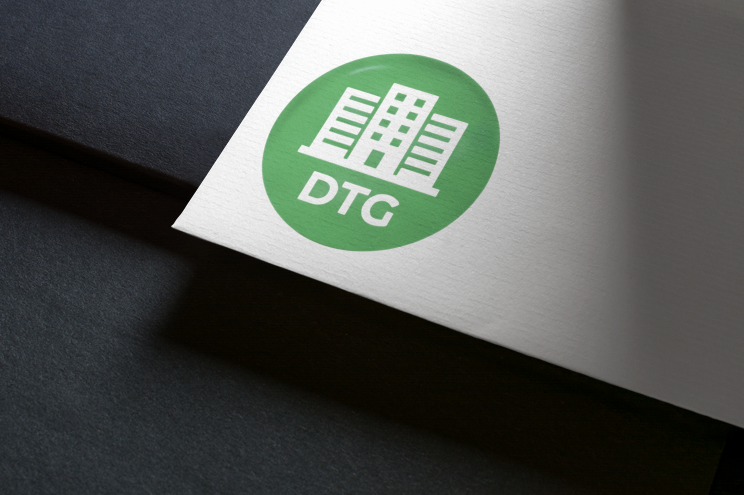 Logo circulaire vert avec icône de bâtiment et inscription « DTG » sur papier blanc sur fond noir.