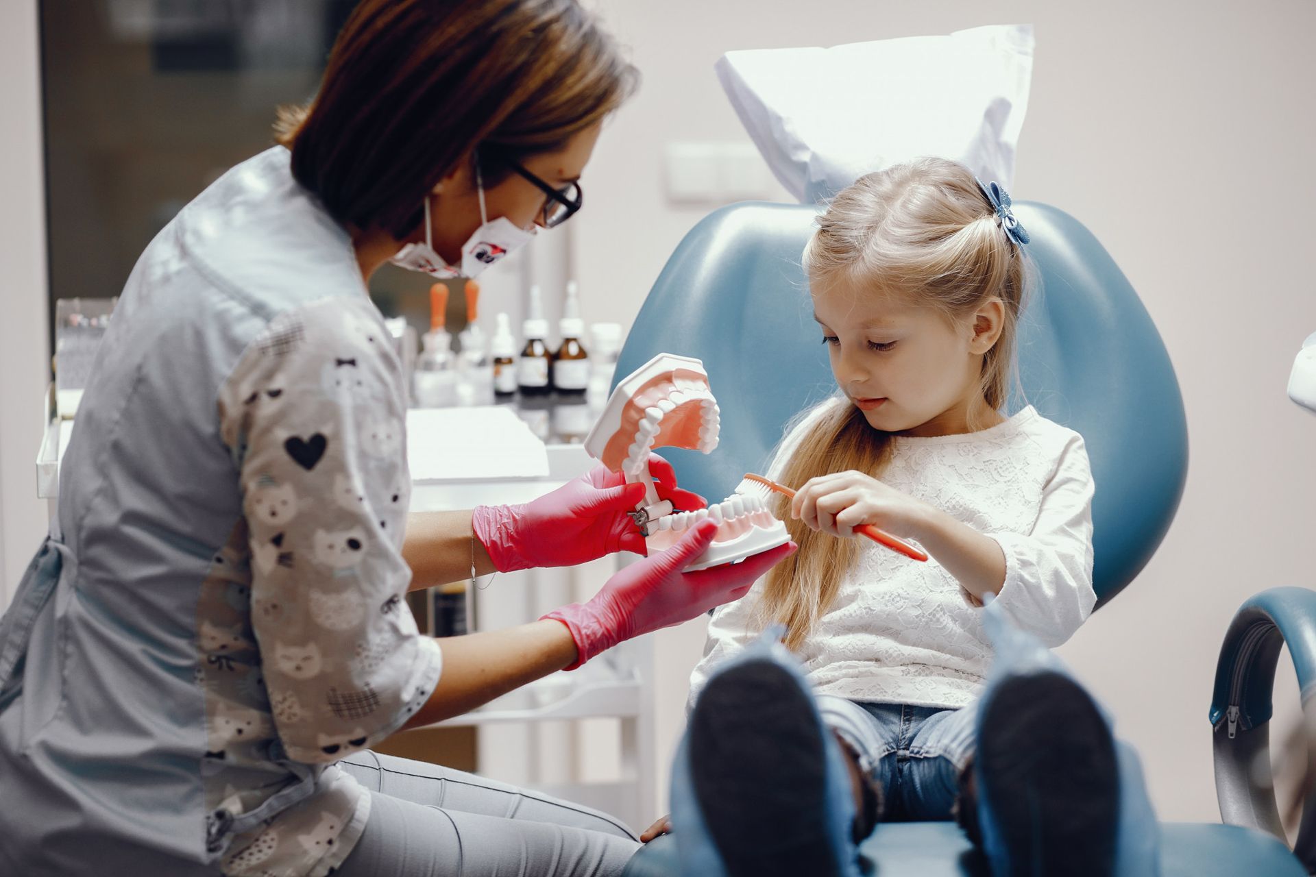 A little girl is brushing her teeth at the dentist.