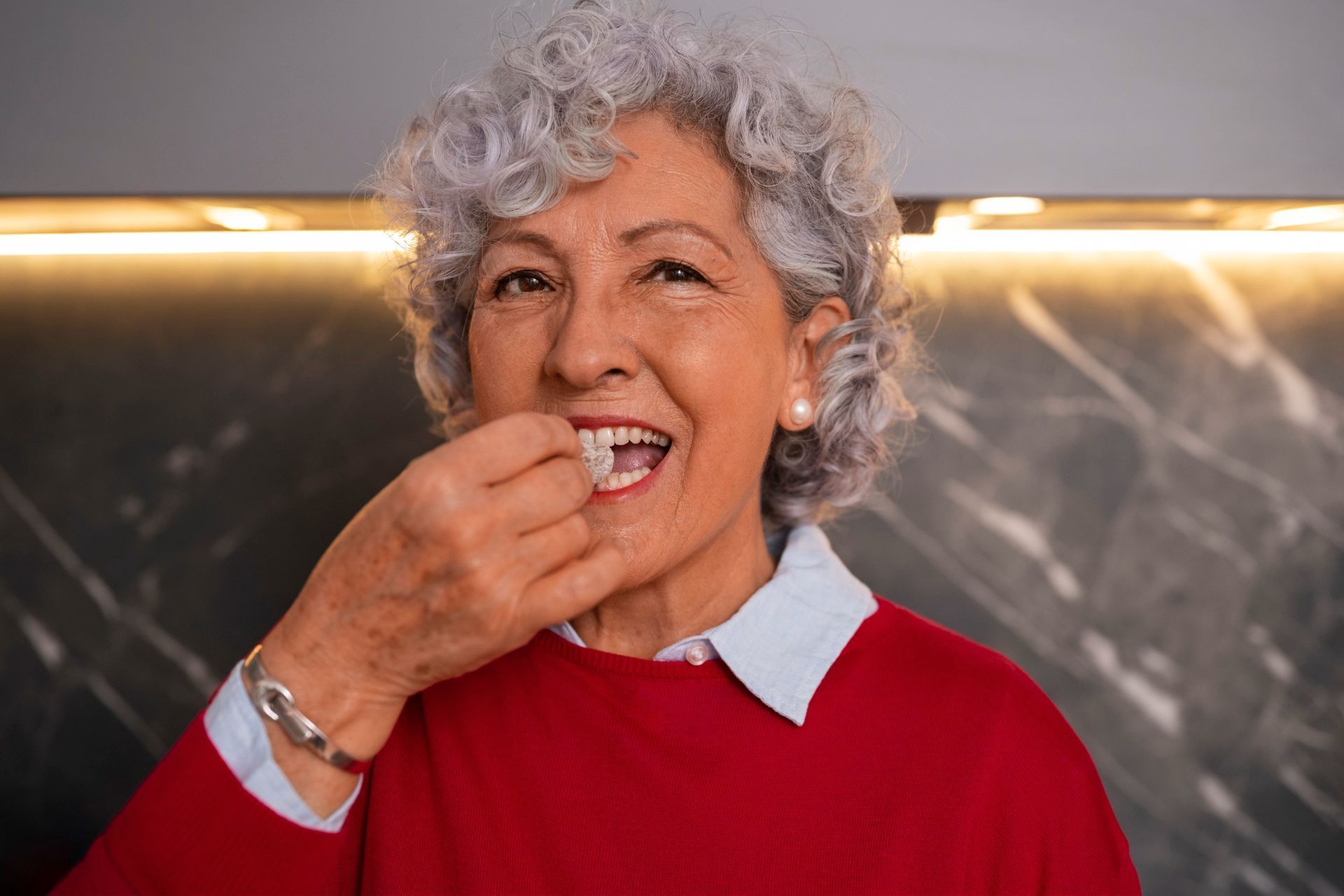 An elderly woman in a red sweater is eating something.