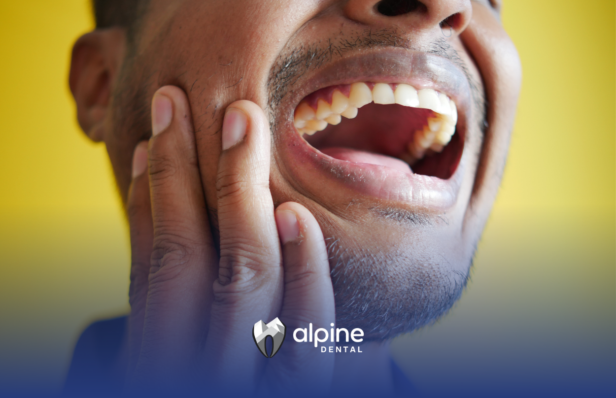 Man with hand on cheek, mouth open, showing teeth, in pain.