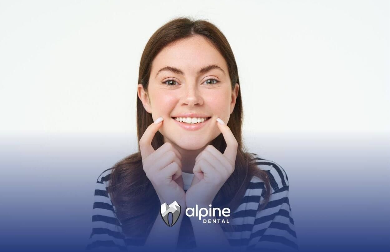 Smiling woman pointing at her teeth with both hands.
