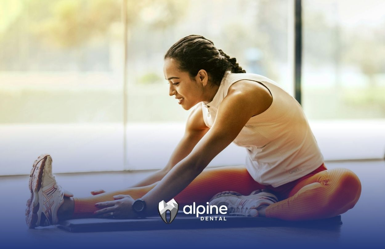 Woman stretching on a mat in workout clothes inside a gym days after a dental crown procedure in NJ.