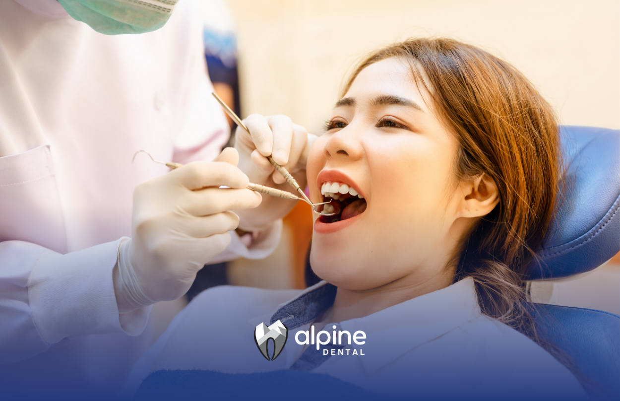 A dentist examining a woman's teeth with dental instruments in a dental clinic. The woman is smiling.