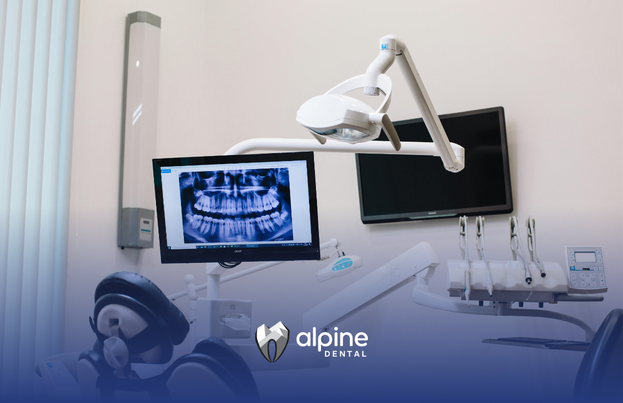 Dental office interior, showing an X-ray on a monitor above the dental chair and instruments. The room is clean and white.