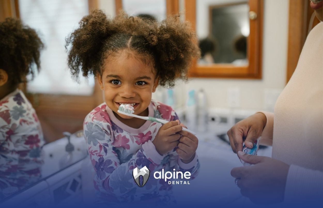 Young girl smiling while brushing her teeth with help from an adult at the bathroom in Lakewood, NJ.