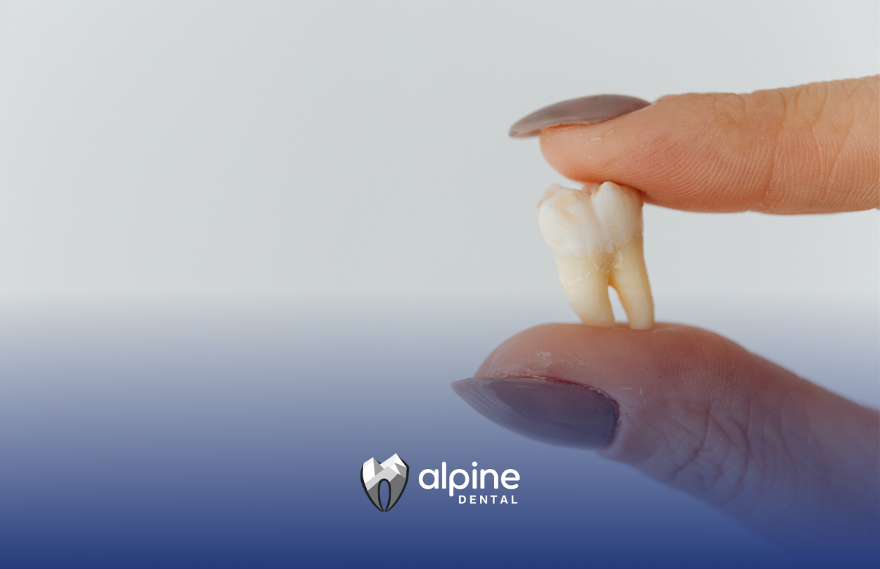 A hand holding a removed tooth; light blue background, Alpine Dental logo.