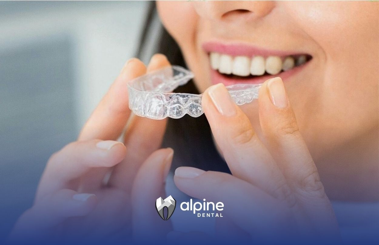 Smiling woman holding a clear dental aligner with both hands at a dental clinic in Lakewood, NJ.